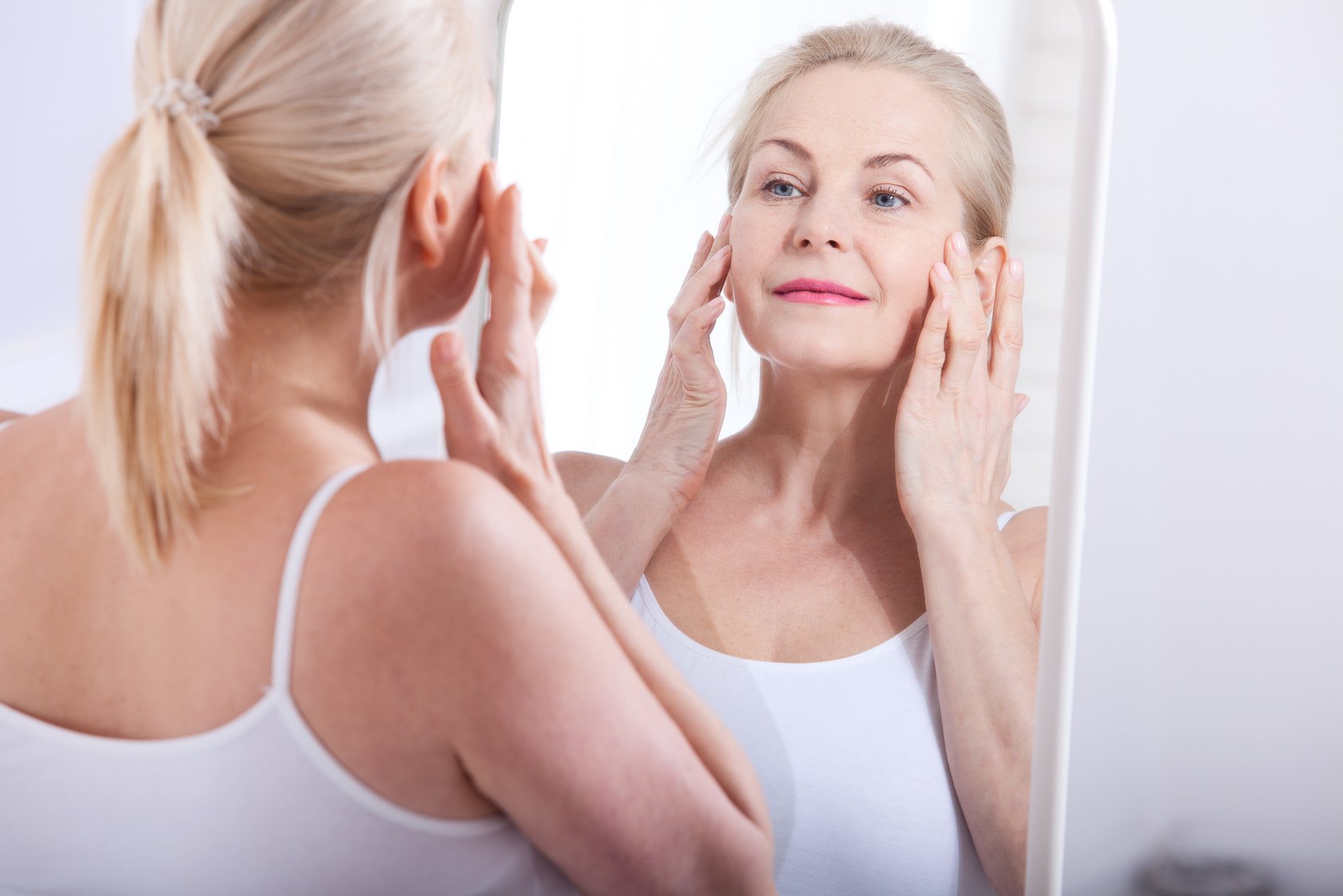 Middle aged woman looking at wrinkles in mirror. Plastic surgery and collagen injections. Makeup. Macro face. Selective focus